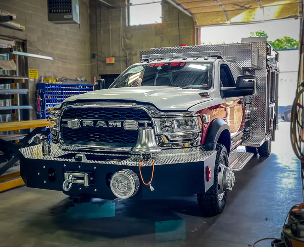 Exterior view of small fire truck showing cab, body compartments, and wheel/tire area.